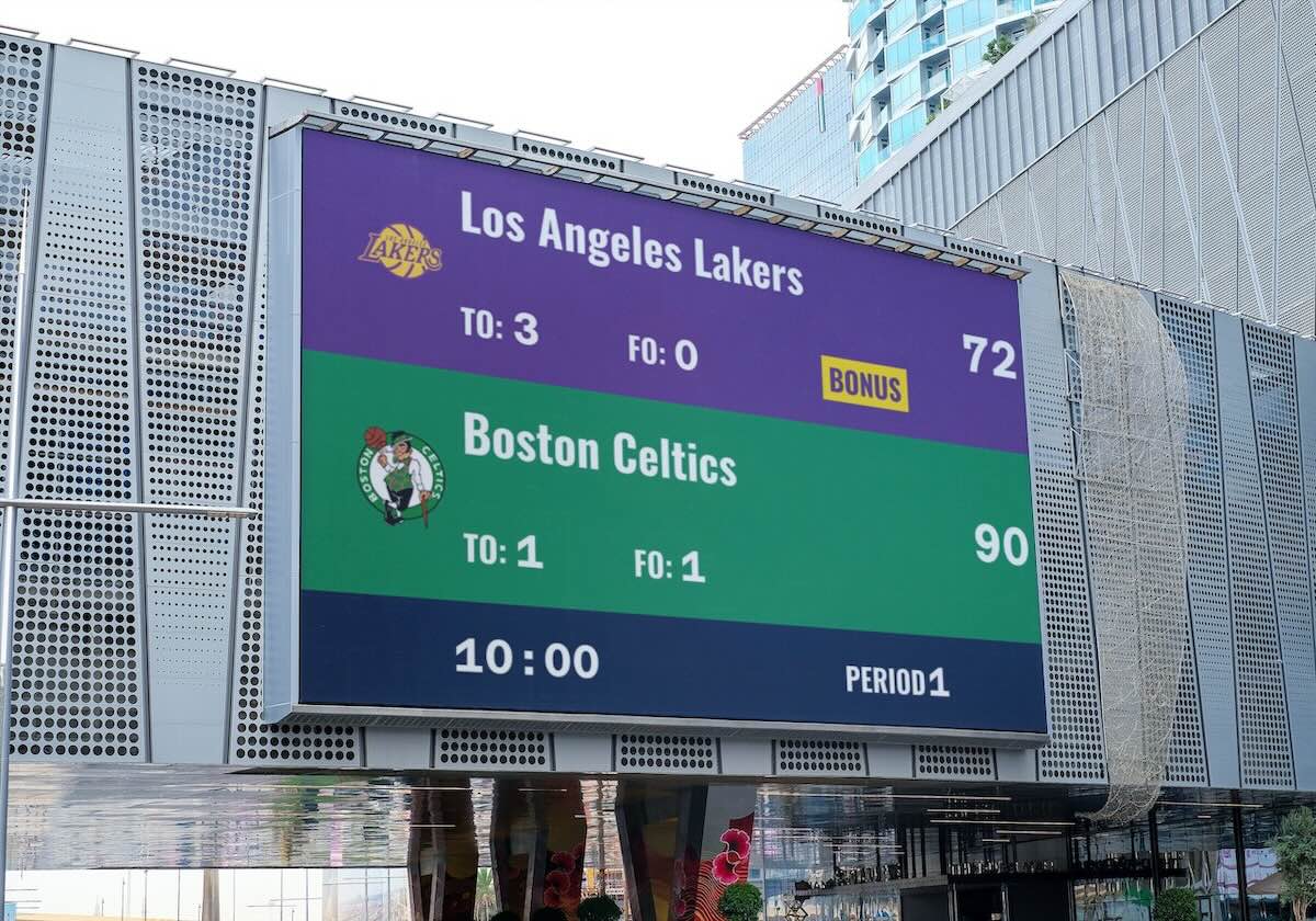 A sports scoreboard being shown on a large TV that is attached to the outside of a building.